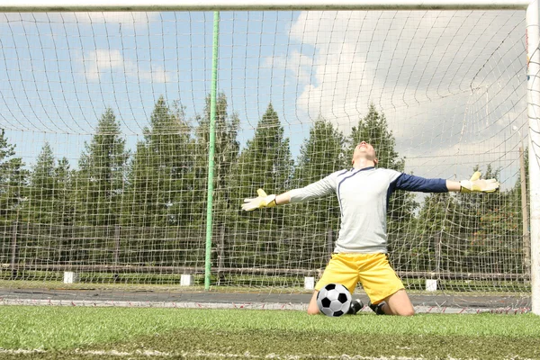 Full length portrait of Goalkeeper in uniform with smiley face. Man standing on fresh green grass football field