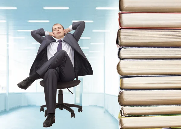 Relaxed businessman with hands behind his head by stack of books