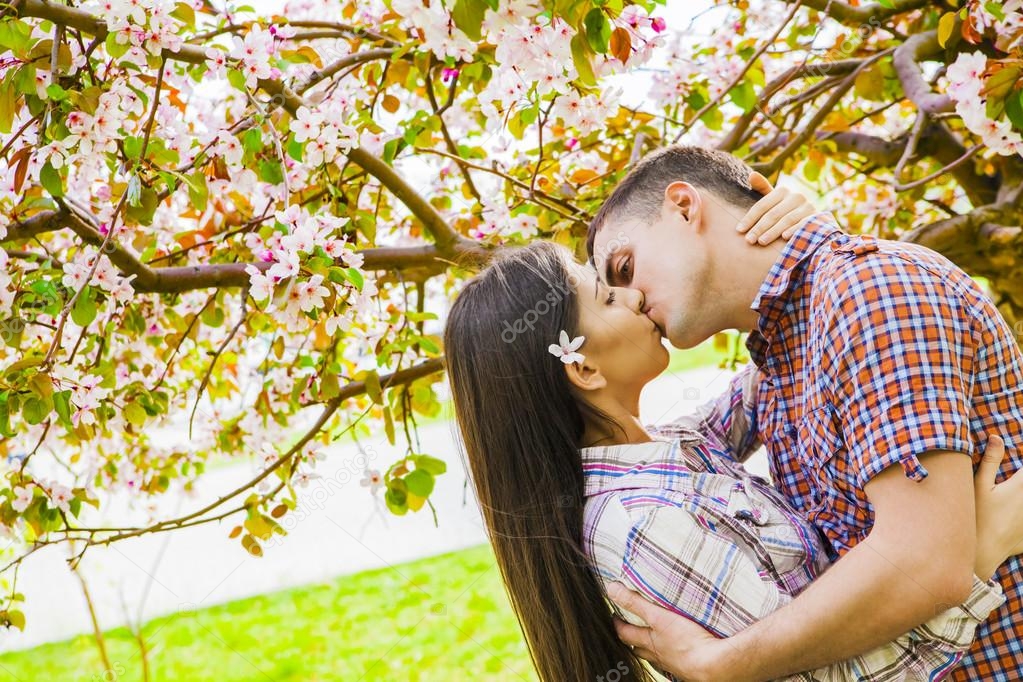 Loving couple under blossoming branches lissing 