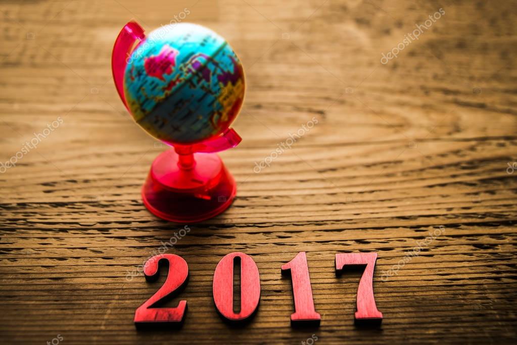 Earth globe with numerals twenty seventeen on brown wooden background