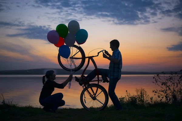 Silhouette of couple Man with  bicycle and  Woman holding  colorful balloons on sunset cloudy sky