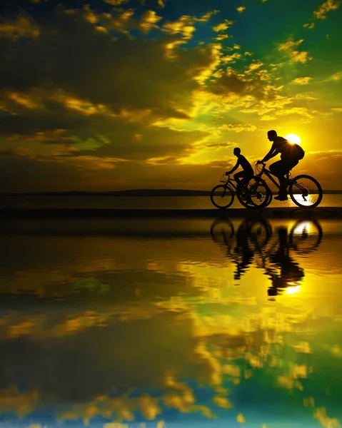 Menschen Silhouetten Auf Fahrrädern Mit Reflexion Wasser Auf Sonnenuntergang Hintergrund — Stockfoto