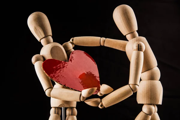 Wooden mannequins holding a red heart.
