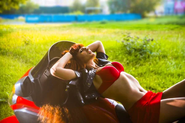 田舎道に赤のモダンなバイクに横たわる若い赤毛のバイカー女 — ストック写真