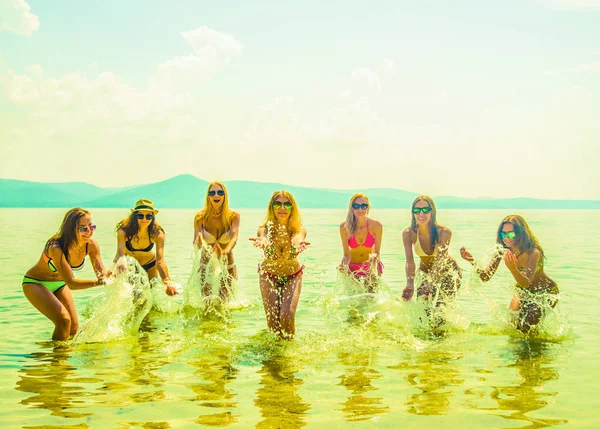 年轻的一群妇女在日落时分在海里跳跃 在水中跳跃的成年女孩队 — 图库照片