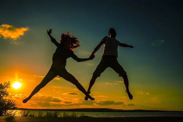 カップルの女の子と男の子のビーチでジャンプのシルエット — ストック写真