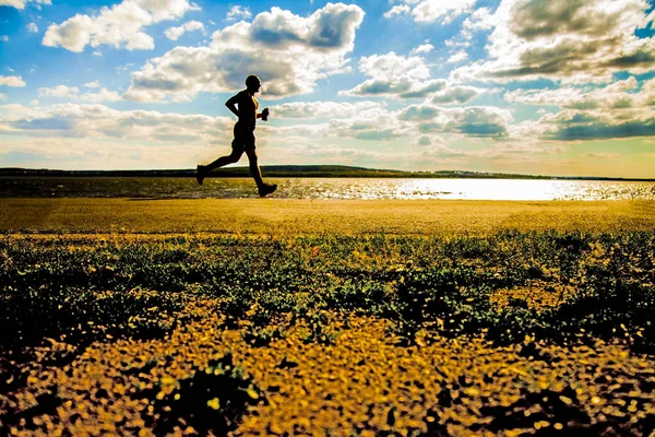 Silhouette eines laufenden Mannes in Sonnenstrahlen am Strand. Sportler in Sho — Stockfoto