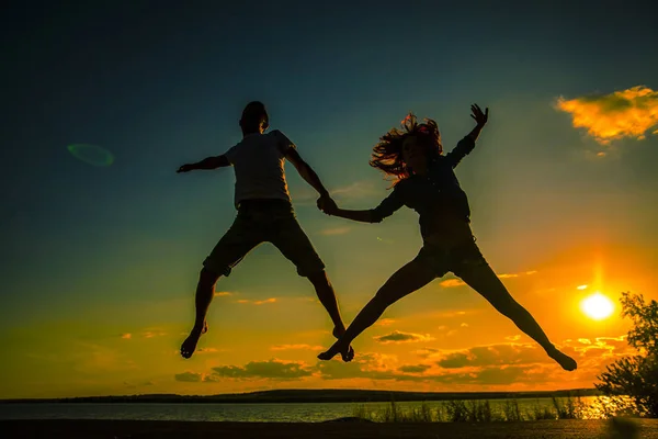 カップルの女の子と男の子のビーチでジャンプのシルエット — ストック写真