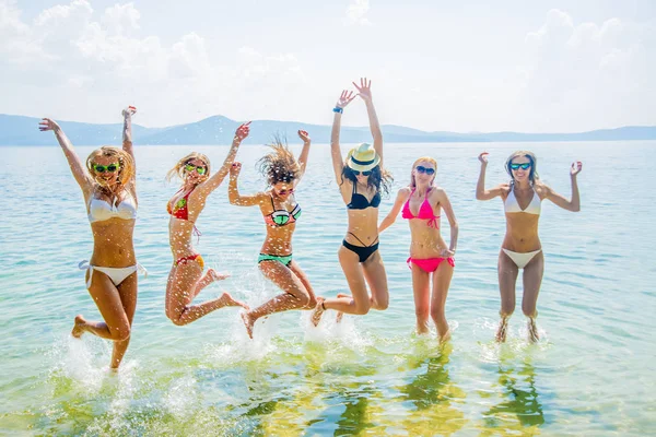 young group of women  jumping in ocean at sunset. Team of adult girls jumping  in water
