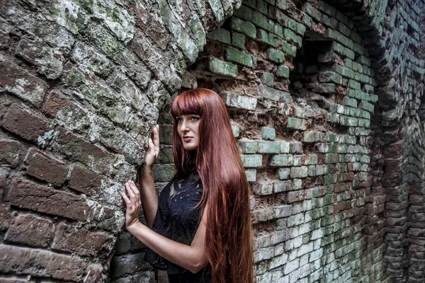 sad redhead woman in black luxury summer dress leaning  on old retro vintage aged brick wall