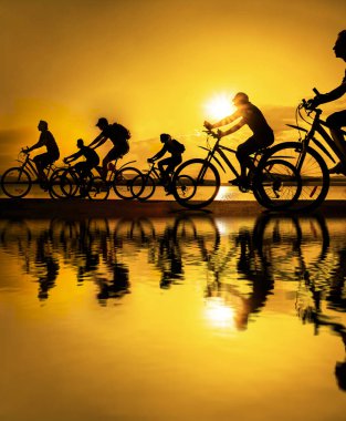 Boşluk. Gün batımında bisiklete binen sportif arkadaşlar. Bisikletçiler sahil boyunca gidiyor. Doğa arka planında spor.