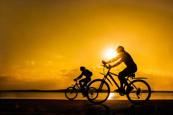 运动的朋友在自行车在日落 在海岸骑自行车的剪影 体育在自然背景 — 图库照片