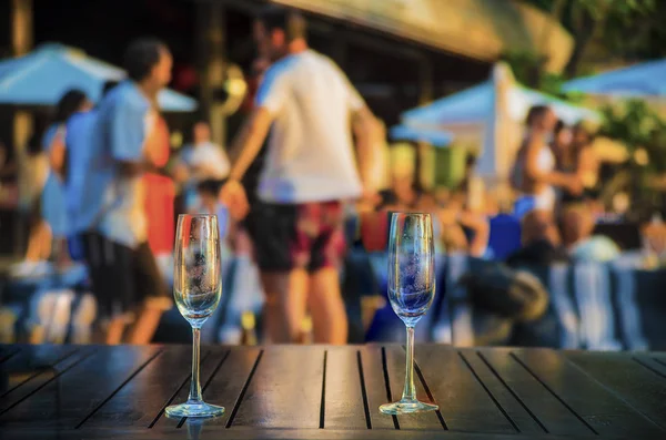 glasses  against group of dancing people. Hot beach party. Sexy people. focus on empty transparent glasses