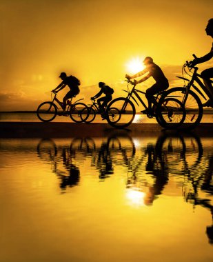 Boşluk. Gün batımında bisiklete binen sportif arkadaşlar. Bisikletçiler sahil boyunca gidiyor. Doğa arka planında spor.