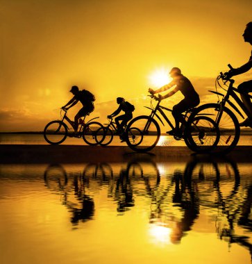 Boşluk. Gün batımında bisiklete binen sportif arkadaşlar. Bisikletçiler sahil boyunca gidiyor. Doğa arka planında spor.