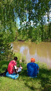 macera, seyahat, turizm ve insan kavramı - akustik gitar ile iki adam geri görünümü ve Rusya'da yaz ormanına karşı kamp nehir bakıyor