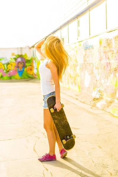 teen girl holding  long skate board stand against  wall.