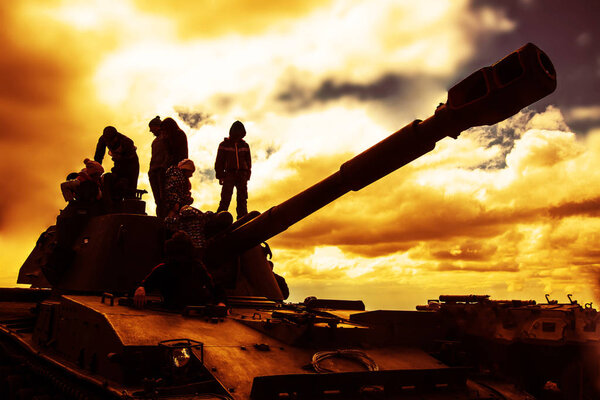 A group of soldiers against the dawn. Silhouette of an army soldiers preparing  tank and weapons at sunset. 