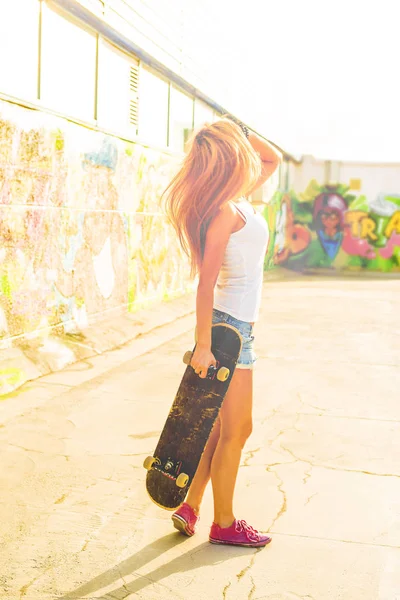 teen girl holding  long skate board stand against  wall.