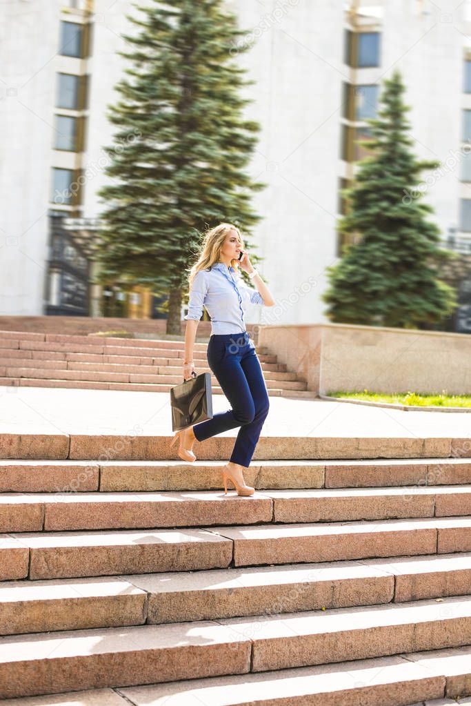 busy blond businesswoman talking on mobile phone on city street background. active Business woman walk downstairs 