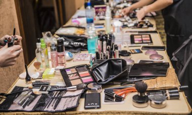 Makyöz elleri. Masada dekoratif kozmetik seti var. Salondaki bir masanın üzerinde bir sürü farklı kozmetik ve fırça var. Güzellik salonunda çalışıyorum. Ahşap işyerinde renkli kozmetik ürünler. Göz farı, kızarma, toz, profesyonel kozmetik ve makyaj. 