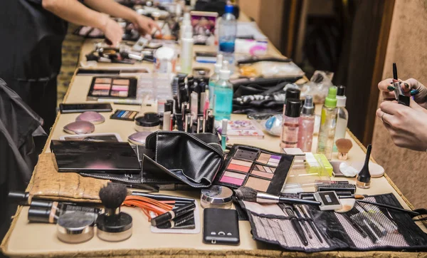 hands of make up artist. Set of decorative cosmetics on table. Many different cosmetics and brushes on a table in the salon. Work in a beauty salon. Colorful cosmetics on wooden workplace. Eye shadow, blush, powder, professional cosmetics and makeup