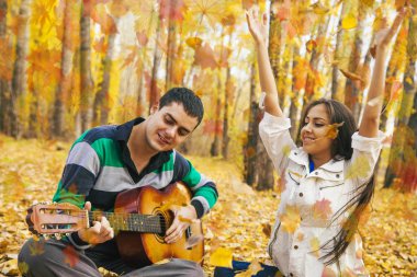 Genç Latin asıllı şirin kız ve arka planda sarı sonbahar orman uçan ile akustik gitar çalmak adam portresini bırakır.