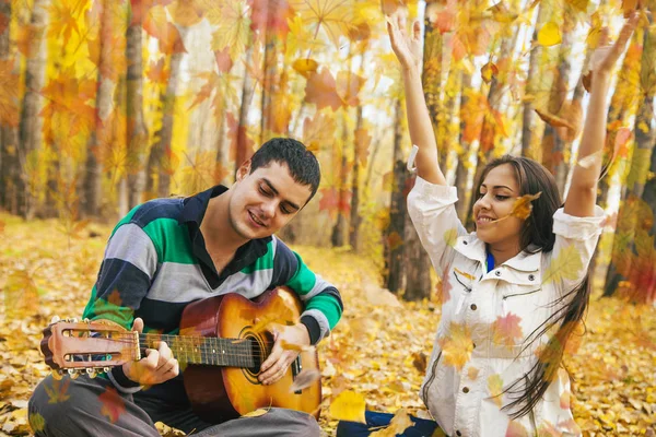 Genç Latin asıllı şirin kız ve arka planda sarı sonbahar orman uçan ile akustik gitar çalmak adam portresini bırakır.