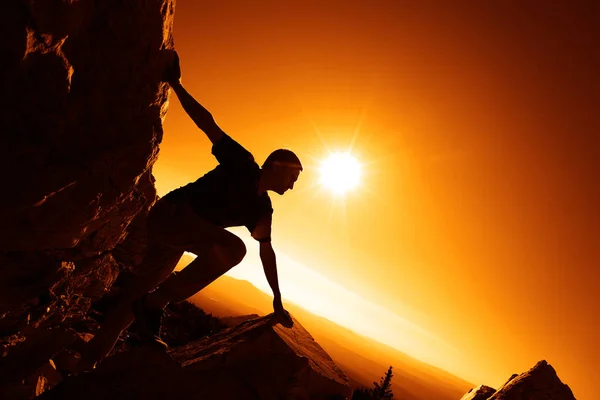 Silhouette of a man climbing on top of a mountain against  sunrise.