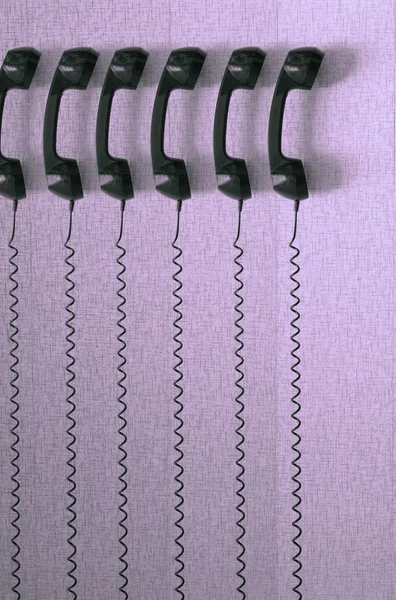 Black plastic telephones hanging by cords on purple background