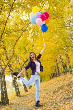 El diğer bacakla tek ayak üzerinde duran ve balonlar tutan genç kız