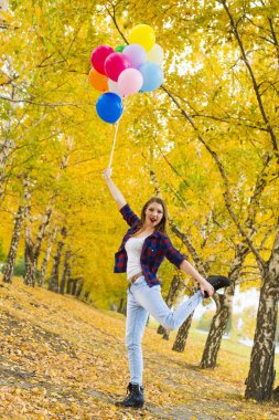 El diğer bacakla tek ayak üzerinde duran ve balonlar tutan genç kız