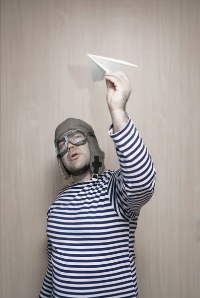 Adult man  in aviator helmet, pilot hat and protective glasses playing with  paper plane.