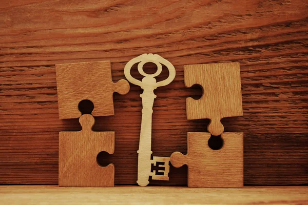 wooden key between puzzle pieces, business concept