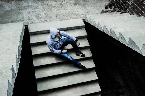 Sad Teenager on concrete stairway. Young, musculate man sitting on the stairs