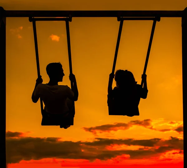 Back light portrait of a couple silhouette sitting on swing watching a sunrise on the beach with the sun in a warmth background.