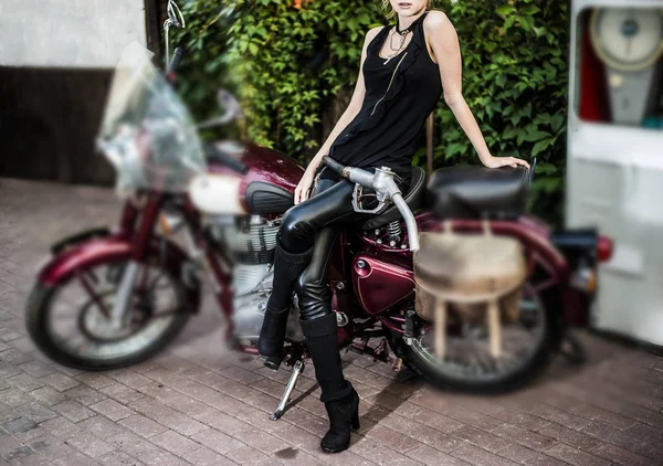 Biker girl on vintage retro motorcycle against gasoline station