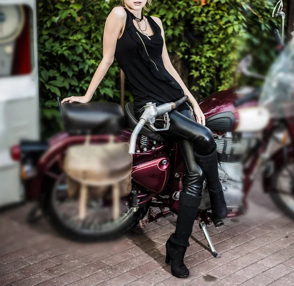 Biker girl on vintage retro motorcycle against gasoline station