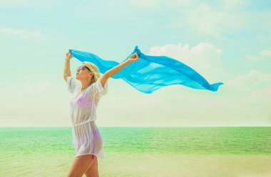 Kadın yaz sahilde poz. Beyaz plaj elbiseli sarışın kız. Mavi bezle sahilde genç güzel kadın