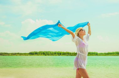 Kadın yaz sahilde poz. Beyaz plaj elbiseli sarışın kız. Mavi bezle sahilde genç güzel kadın