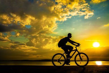 Genç adam bisikletçi Sunset'teki silüeti 