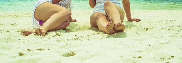 专注于腿部 妇女坐在白色热的沙子反对热带海滩 — 图库照片
