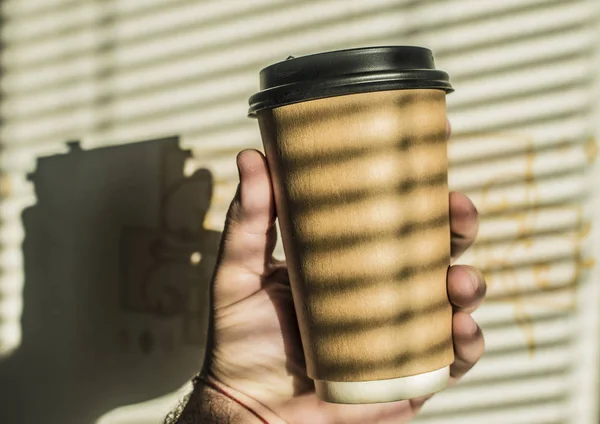 Paper cup of coffee in man's hand with  jalousie shadow.  empty space for text