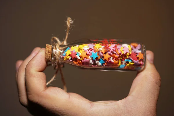 カラフルなキャンディー星と小さなガラスの瓶を持っている手 — ストック写真
