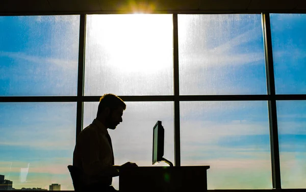 silhouette of business man on background office room window with  beautiful sunset sky. Businessman working  pc compute
