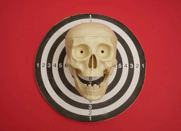 Dart board with human skull placed on red background
