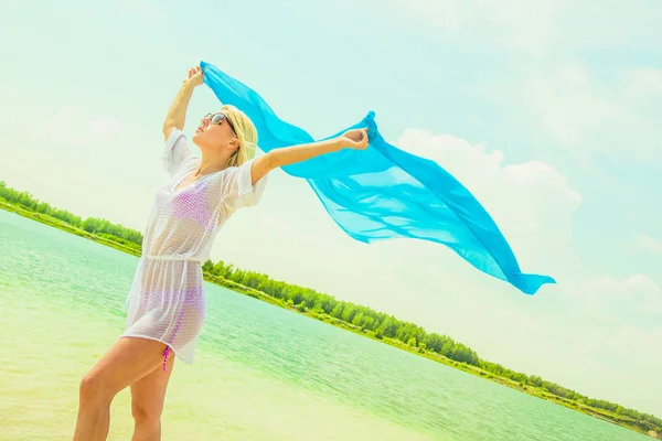 在夏日海滩上假扮的女人穿着白色沙滩裙的金发女郎年轻美丽的妇女在海滩与蓝色布料 — 图库照片