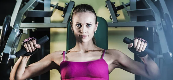 Sports woman doing exercises on power training machine  in the gym.