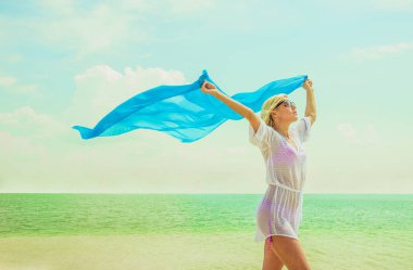 Kadın yaz sahilde poz. Beyaz plaj elbiseli sarışın kız. Mavi bezle sahilde genç güzel kadın