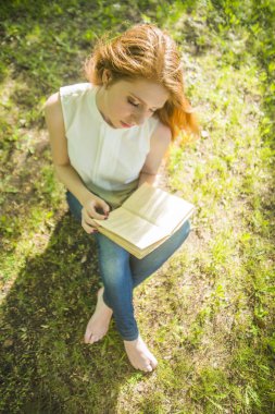 Üstten Görünüm. Taze yeşil çimenlerin üzerinde otururken kitap okuma kız.
